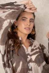 Camisa oversize con estampado abstracto en tonos marrones y beige, cuello mao y cierre frontal con botones. Presenta mangas largas anchas con puños abotonados y un corte holgado.