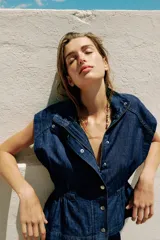 Chaleco de denim azul oscuro con cuello alto, manga sisa y cintura ajustable con elástico. Cierre frontal con botones a presión metálicos.