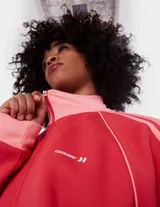 Campera deportiva Coolway de corte suelto (loose fit) con cierre frontal, cuello alto y bolsillos laterales. El cuerpo principal es rojo vibrante y los puños, cuello y detalles de las mangas son de color rosa claro, con dos franjas del mismo rosa claro a lo largo de las mangas.