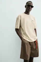 Camiseta relaxed fit color beige, con cuello redondo y manga corta. Presenta un bordado y estampado combinado a contraste en el delantero y la espalda.