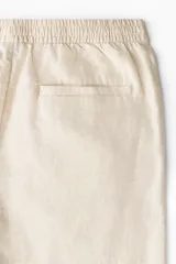 Pantalón de corte regular fit confeccionado en mezcla de lino y algodón, color beige. Presenta cintura elástica con cordón ajustable, cierre de botón y bolsillos laterales.