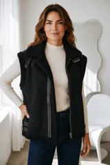 Chaleco estilo gamulán de color negro, confeccionado en material tipo gamuza con interior y bordes de corderito sintético. Presenta cierre frontal metálico, cuello solapa y detalles de correas con hebillas en los hombros y laterales.