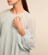 Blusa de crepé en color verde agua claro, con cuello redondo y mangas largas voluminosas. Presenta un diseño con textura plisada tanto en las mangas como en el cuerpo de la prenda, con puños ajustados.