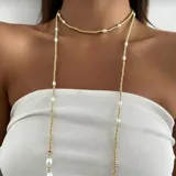 Collar largo tipo lariat, compuesto por una cadena fina de cuentas doradas y perlas blancas irregulares intercaladas. El diseño permite llevarlo como gargantilla corta y como collar largo.