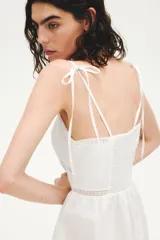 Vestido midi de algodón color blanco, con escote halter y breteles para atar en la nuca. Presenta detalles de encaje en el escote y la cintura, y falda fruncida con leve vuelo.