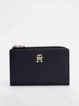 Billetera plegable Tommy Hilfiger color azul marino, de acabado granulado, con cierre de botón a presión, múltiples ranuras para tarjetas, compartimento para billetes y bolsillo exterior con cremallera. Presenta el monograma TH metálico en la parte delantera.