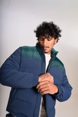 Campera puffer con diseño bicolor, cuerpo en azul marino y canesú superior en verde oscuro. Presenta cuello alto, cierre frontal completo y puños elásticos.