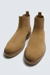 Bota estilo Chelsea de hombre, color marrón, fabricada en piel con acabado serraje (gamuza). Presenta elásticos laterales oscuros y suela de goma a tono con tacón bajo.