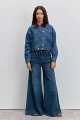 Cazadora de denim azul con corte cropped y diseño de doble botonadura frontal. Presenta un cuello de pana en color bordó y botones metálicos dorados.