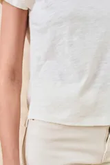 Remera blanca de algodón con escote en V y mangas cortas. Presenta un diseño estampado o bordado en negro de estilo tribal o geométrico en los laterales y mangas.