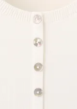 Chaleco de punto fino y diseño entallado, color marfil, con cuello redondo, manga corta y cierre frontal con pequeños botones.