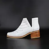 Botín de cuero blanco con textura croco, calados circulares y aberturas laterales en forma de V. Taco foliado de suela natural y vira cosida.