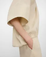 Blusa globo amplia de color beige con escote barco y manga corta japonesa. Presenta bajo abullonado con elástico interior.