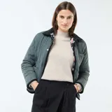 Chaqueta corta con estampado floral en tonos rosa y celeste sobre fondo negro. Tiene cuello mao y cierre frontal con botones a presión.
