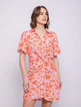Vestido corto de viscosa con estampado floral multicolor, de manga corta, con cuello camisero y cierre frontal abotonado. Presenta un nudo decorativo en la cintura.