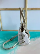 Cartera de cuero blanca y dorada con solapa texturizada tipo cocodrilo y detalles pintados a mano. Cuenta con doble asa de mano, correa ajustable, herrajes metálicos y cierre superior.
