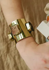 Brazalete rígido de bronce con diseño ancho y acabado pulido, decorado con piedras naturales de textura rugosa engarzadas en el metal.