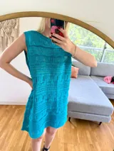 Vestido corto de algodón color turquesa, sin mangas y con cuello redondo. Presenta un tejido calado con diferentes patrones de punto.
