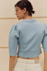 Chaqueta celeste de punto con cuello redondo, mangas cortas abullonadas y cierre frontal de botones.