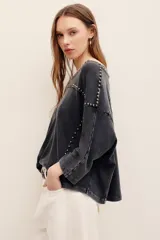 Remera de algodón negro con efecto deslavado, cuello redondo y mangas cortas. Presenta aplicaciones de tachas metálicas en el escote, hombros y a lo largo del frente.