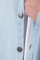 Chaqueta de denim celeste de corte relajado, con cuello clásico, cierre frontal con botones metálicos y un bolsillo aplicado en el pecho.
