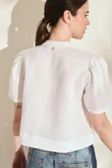 Blusa de lino color amarillo, con cuello mao, cierre frontal con cremallera y mangas cortas abullonadas. Cuenta con un bolsillo aplicado en el frente.