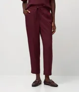 Pantalón de crepé rojo, modelo estilo pijama, de corte fluido, con cintura elástica y lazo de ajuste con terminales metálicas. Cuenta con bolsillos laterales y cierre frontal con cremallera y botón.