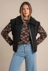 Chaleco estilo gamulán de color negro, con interior y detalles de corderito sintético. Presenta cierre frontal, cuello solapa y bolsillos laterales.