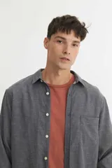 Camisa de corte regular fit, confeccionada en algodón con textura tramada en dos tonos de azul. Presenta cuello solapa clásico, cierre frontal con botones personalizados y un bolsillo aplicado en el pecho con detalle de logo bordado.