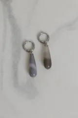 Aros tipo argolla de acero quirúrgico con dije colgante en forma de gota de piedra natural en tonos grisáceos.