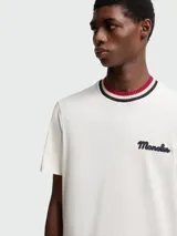 Camiseta de manga corta color blanco hueso con cuello redondo de punto acanalado a rayas en tonos rojo, azul marino y blanco. Presenta un pequeño logo bordado en azul marino en el pecho.