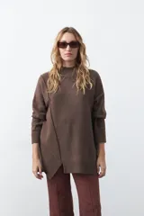 Polera de tejido de punto color marrón, con diseño asimétrico y costura diagonal frontal. Presenta cuello alto, hombros caídos, mangas largas con puños acanalados y ruedo con abertura frontal.