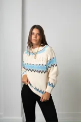 Buzo tejido de punto con diseño de guardas geométricas en tonos celeste y negro sobre base color crema. Presenta cuello redondo, mangas largas y puños acanalados.
