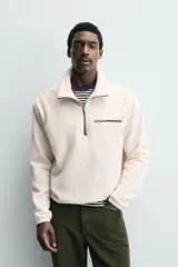Sudadera de tejido polar con textura efecto pelo, corte relajado, cuello subido con cierre frontal de cremallera, manga larga con puños elásticos y bolsillo con cierre en el pecho.