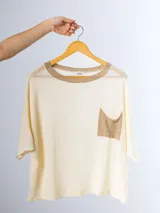 Remera tejida color crema con cuello redondo y bolsillo frontal verde.