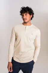 Remera de manga larga tipo Henley, color beige, con cuello redondo y tapeta con botones. Presenta un pequeño logo bordado en el pecho.