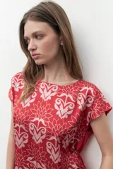 Blusa de satén con estampado floral bicolor en tonos rojo y rosado, de corte recto, cuello redondo y mangas cortas.