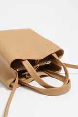 Bolso pequeño de piel vacuna color negro, con estructura rígida, doble asa de mano y correa larga ajustable para llevar al hombro o cruzado. Presenta cierre de botón a presión y logo metálico de la marca en el frente.