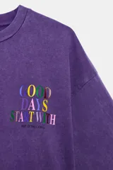 Camiseta corta de efecto lavado, de color morado, con cuello redondo, manga corta y detalle de texto multicolor a contraste en el pecho. Colección especial Fruit of the Loom y Zara.