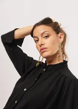 Camisa negra de cuello redondo con frunces y mangas largas con puños abiertos.