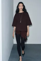 Camiseta de algodón de corte regular, color marrón oscuro o negro, con cuello redondo y manga corta. Presenta un bajo asimétrico con aplicación de encaje negro a tono.