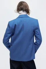 Blazer cruzado celeste de manga larga con solapas de pico, hombreras y bolsillos frontales con solapa. Presenta cierre de doble botonadura con botones oscuros y forro interior.