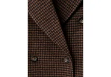 Abrigo de corte sastre con diseño de doble botonadura y solapas amplias. Presenta un estampado de cuadros pequeños en tonos marrones y oscuros, con una silueta estructurada y elegante.