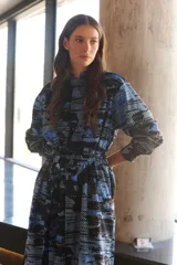 Vestido camisero largo con estampado geométrico en tonos camel y negro. Cuenta con mangas largas con puños, un bolsillo frontal amplio, botones frontales y un botón de cierre en el cuello.