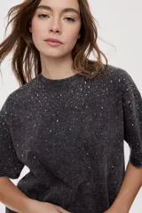 Remera oversized de manga corta y cuello redondo, de color negro con efecto acid wash y aplicación de strass en la parte superior.