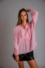 Camisa de color celeste con volados decorativos en el cuello y la parte delantera, cuenta con cordones para ajustar el escote, mangas largas con puños y corte holgado.