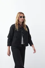 Campera de jean color negro con cuello de pana en tono marrón, cierre frontal con botones metálicos y bolsillos frontales tipo cargo.
