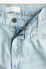 Jean de tiro alto confeccionado en denim de algodón rígido, con diseño curvo y voluminoso en las piernas, tipo barrel. Presenta cinco bolsillos, cierre frontal con botón y detalles de tiras para anudar en los tobillos.