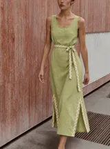 Vestido largo sin mangas color verde, con escote redondo, corte recto y aberturas laterales en el bajo. Cuenta con un cinto ajustable del mismo género con detalles de ondas en color beige, patrón que se repite en las aberturas laterales.