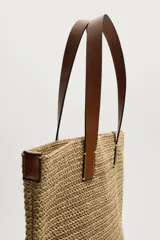 Bolso tipo shopper de acabado trenzado color tostado, con compartimento principal sin cierre, bolsillo plano interior y dos asas de mano de cuero sintético marrón.